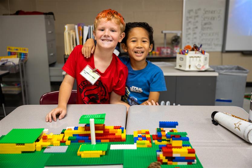 Two boys smile while standing behind a LEGO project
